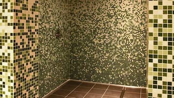 Un espace douche avec des murs recouverts de mosaïques et un sol carrelé de couleur marron.