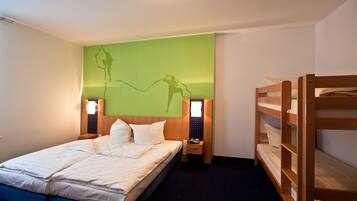 Ein Hotelzimmer mit Etagenbett, einem großen Bett, einer grünen Wand mit Silhouetten-Kunstwerk, Nachttischlampen und einem kleinen Nachttisch.