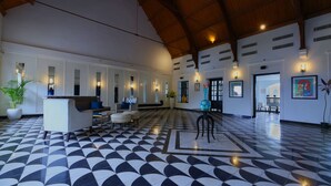 A lobby with a checkered floor, a reception desk, seating area, and a large plant. - Alpha Old Court House (Kochi)