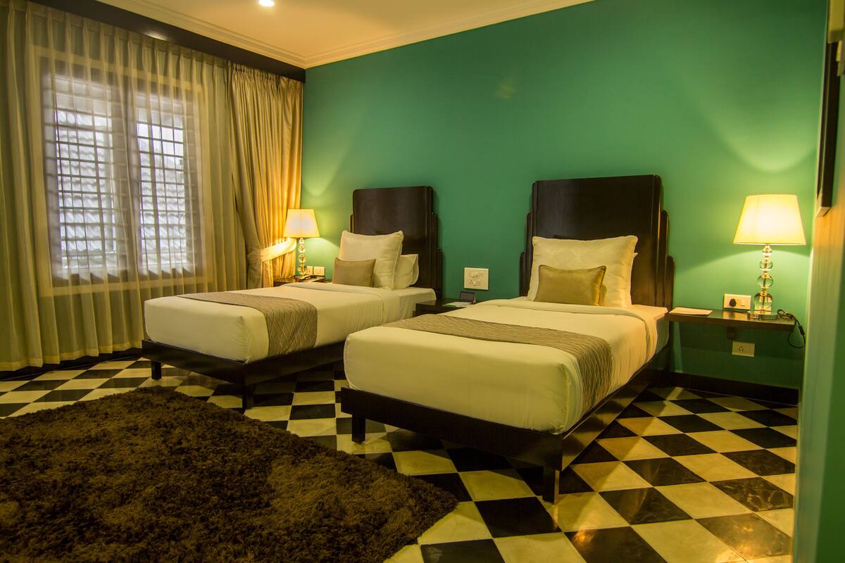 A hotel room with two beds, checkered floor, teal walls, and a large window with curtains.