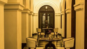 A hotel lobby with a checkered floor, a round dining table with chairs, and a large arched doorway in the background. - Alpha Old Court House (Kochi)