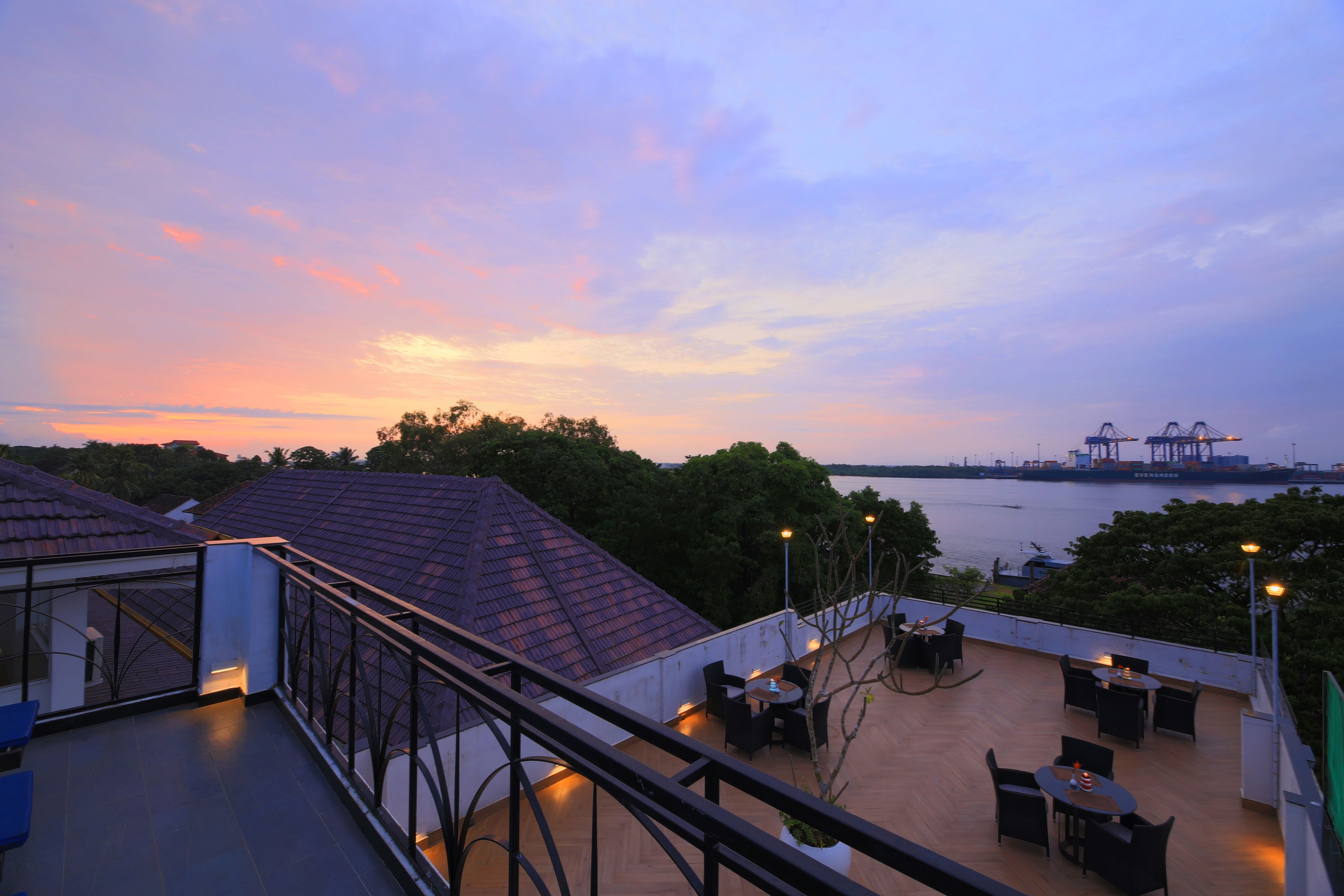 A rooftop terrace with outdoor seating, a view of the water, and a sunset.