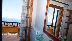 A room with a view of the sea, a table with a chair, a radiator, and a mirror reflecting the room. - Alkmini (Zagora-Mouresi)