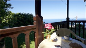 A table with a white tablecloth, two cups of coffee, a white flower, and a basket of cookies on a balcony overlooking a body of water. - Alkmini (Zagora-Mouresi)