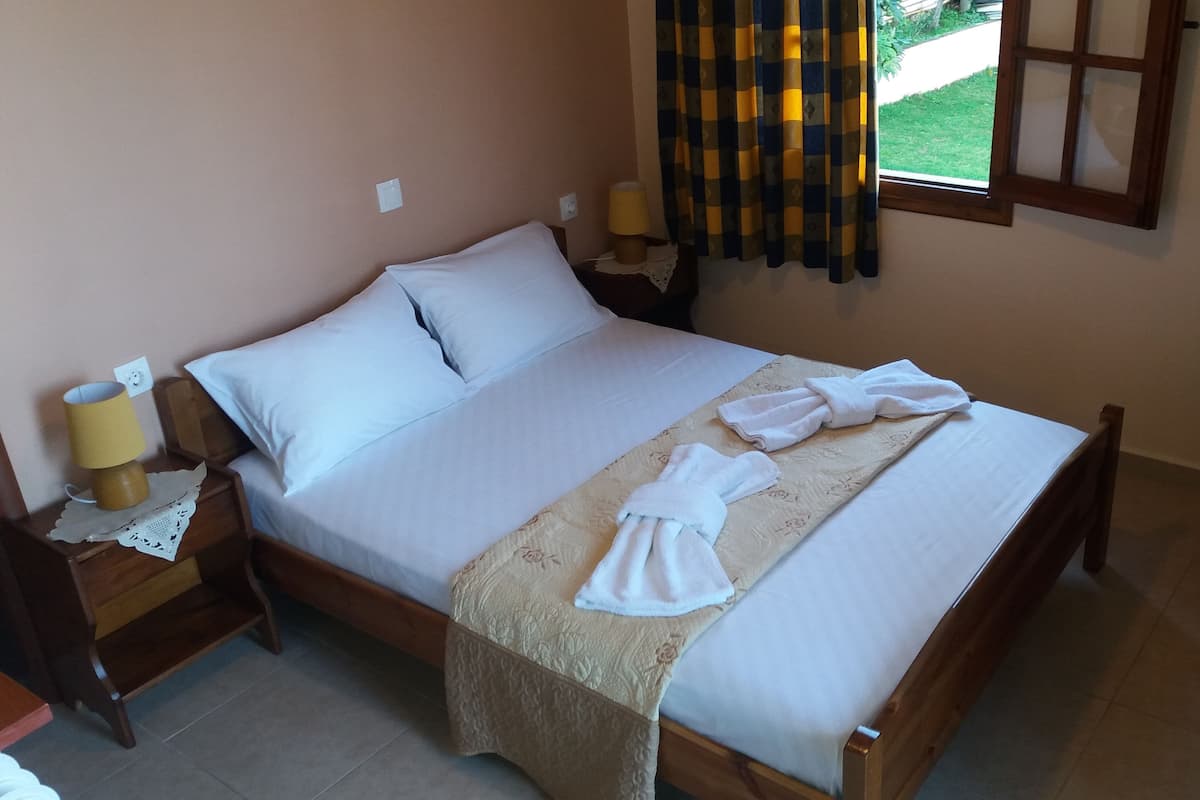 A neatly made bed with white linens, a wooden headboard, and a bedside table with a lamp and a power outlet.