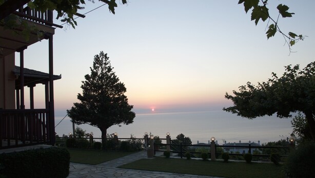 A stone pathway leading to a wooden structure with a view of the sunset over the water. - Alkmini (Zagora-Mouresi)