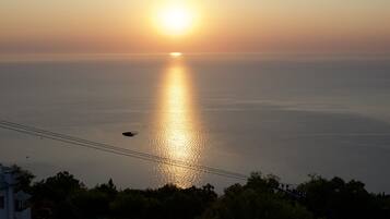 A sunset over a calm sea with a silhouette of a house and trees in the foreground.