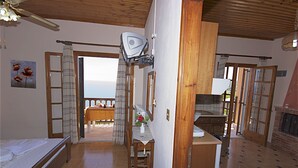 A room with a bed, a desk, a chair, and a small table with a vase of flowers. There is a window with curtains, a ceiling fan, and a view of the outdoors. - Alkmini (Zagora-Mouresi)