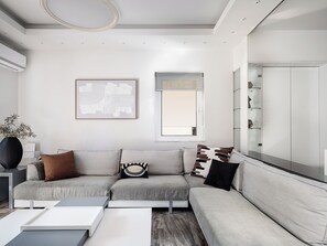 Ein modernes Wohnzimmer mit einem Ecksofa, einem Couchtisch, einem gerahmten abstrakten Kunstwerk und einem großen Fenster.