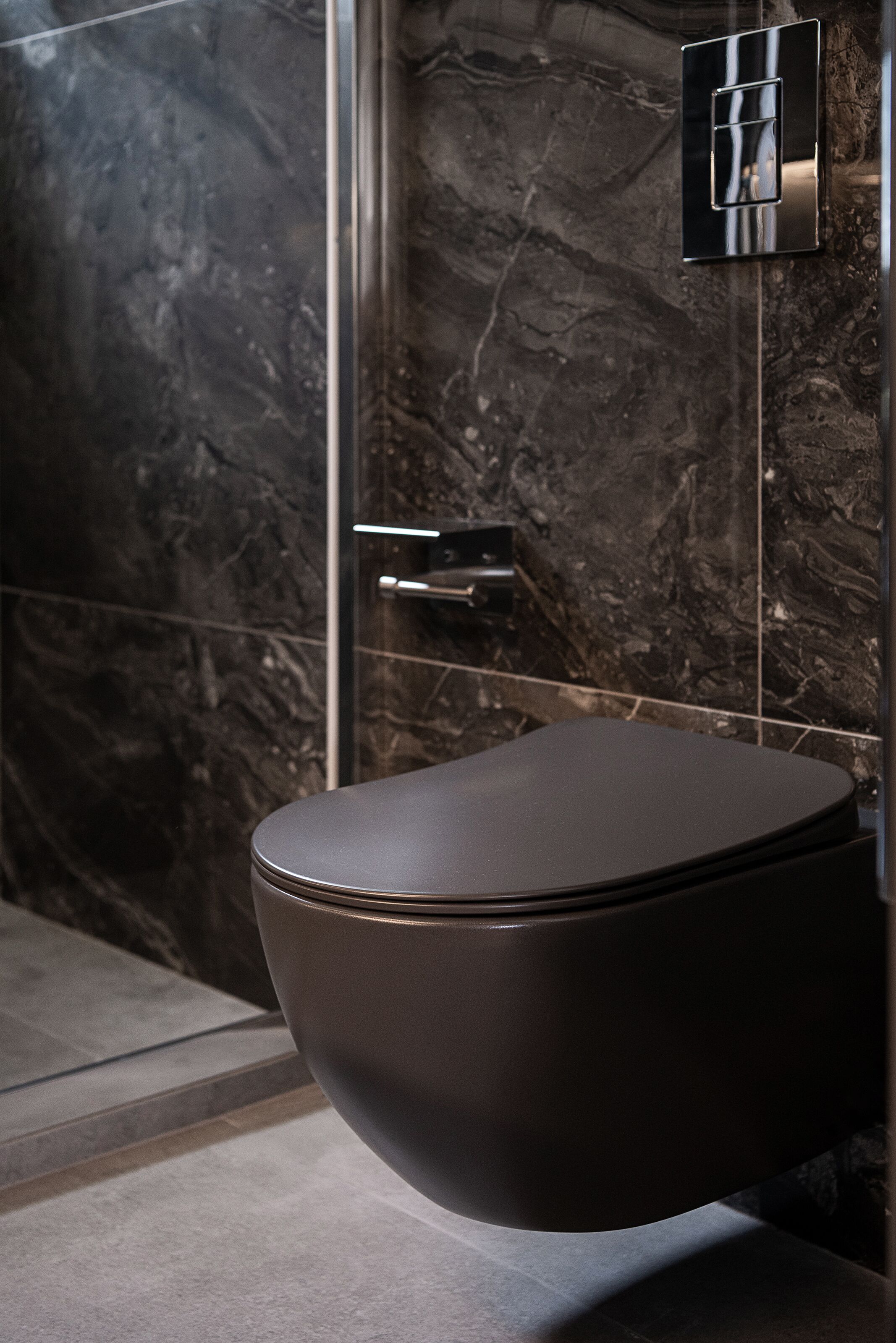 A modern bathroom with a marble wall, a sleek toilet, and a wall-mounted light fixture.