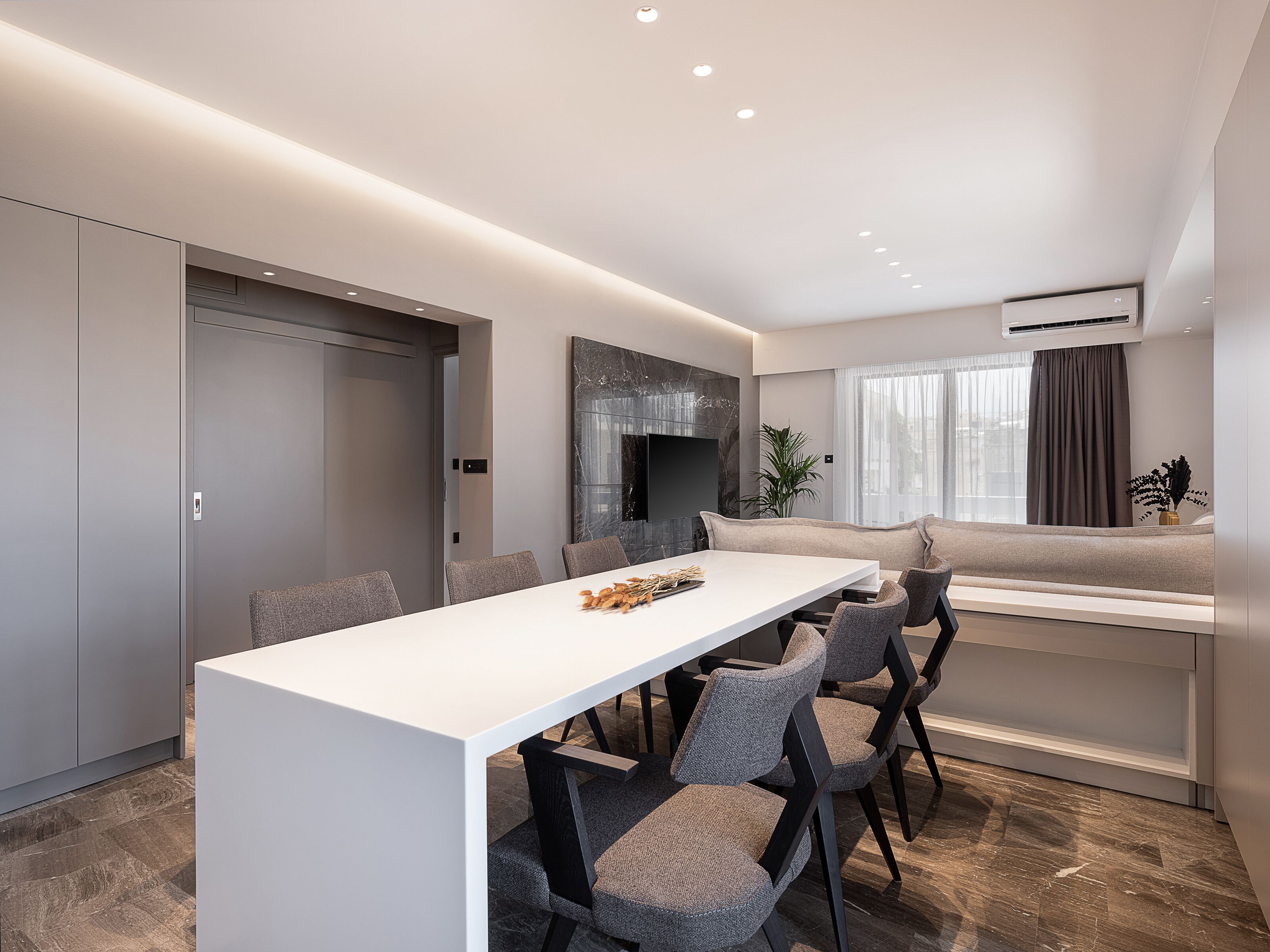 A modern dining area with a white table, grey chairs, and a grey sofa.