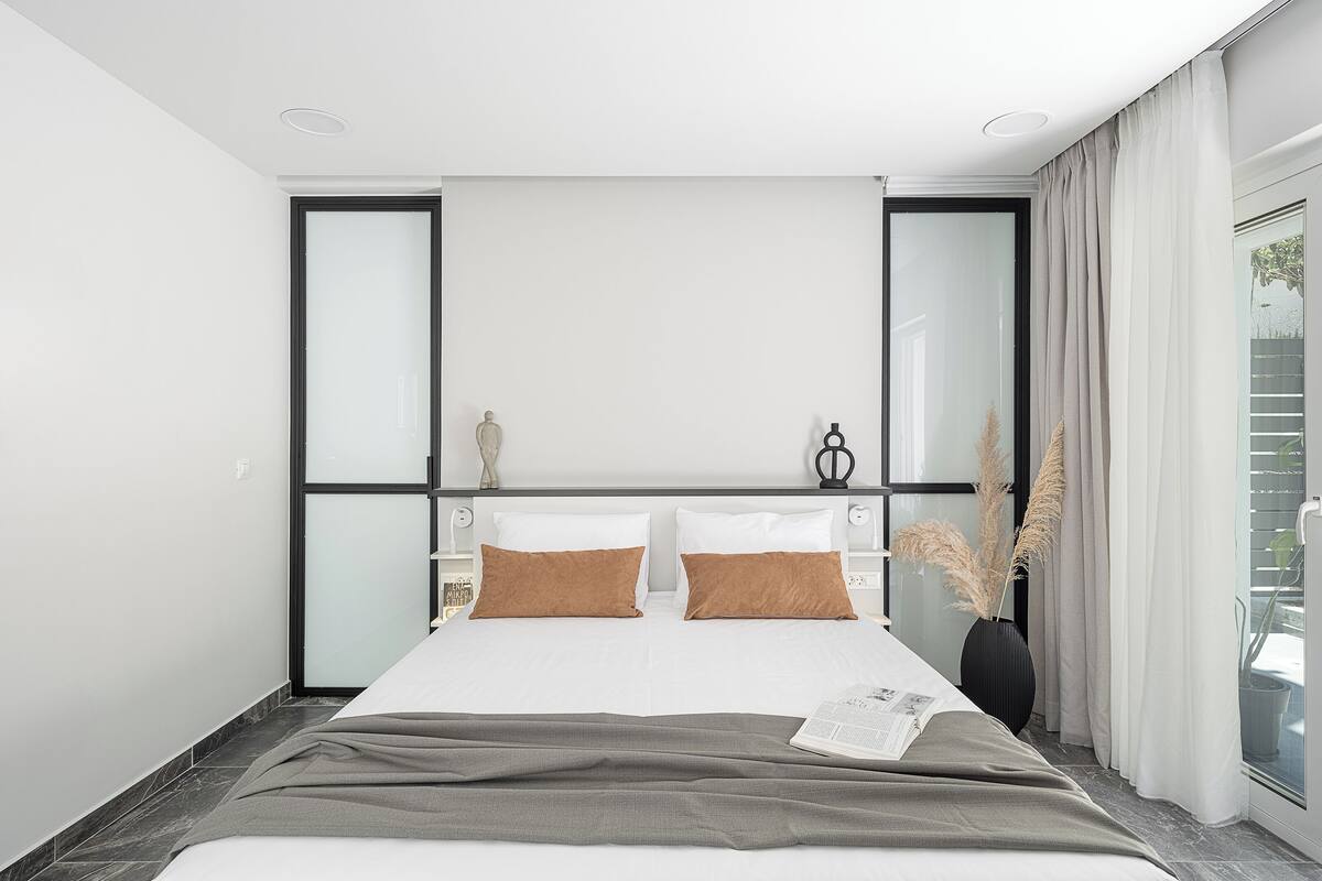 A modern hotel room with a large bed, a bedside table, and a window with curtains.