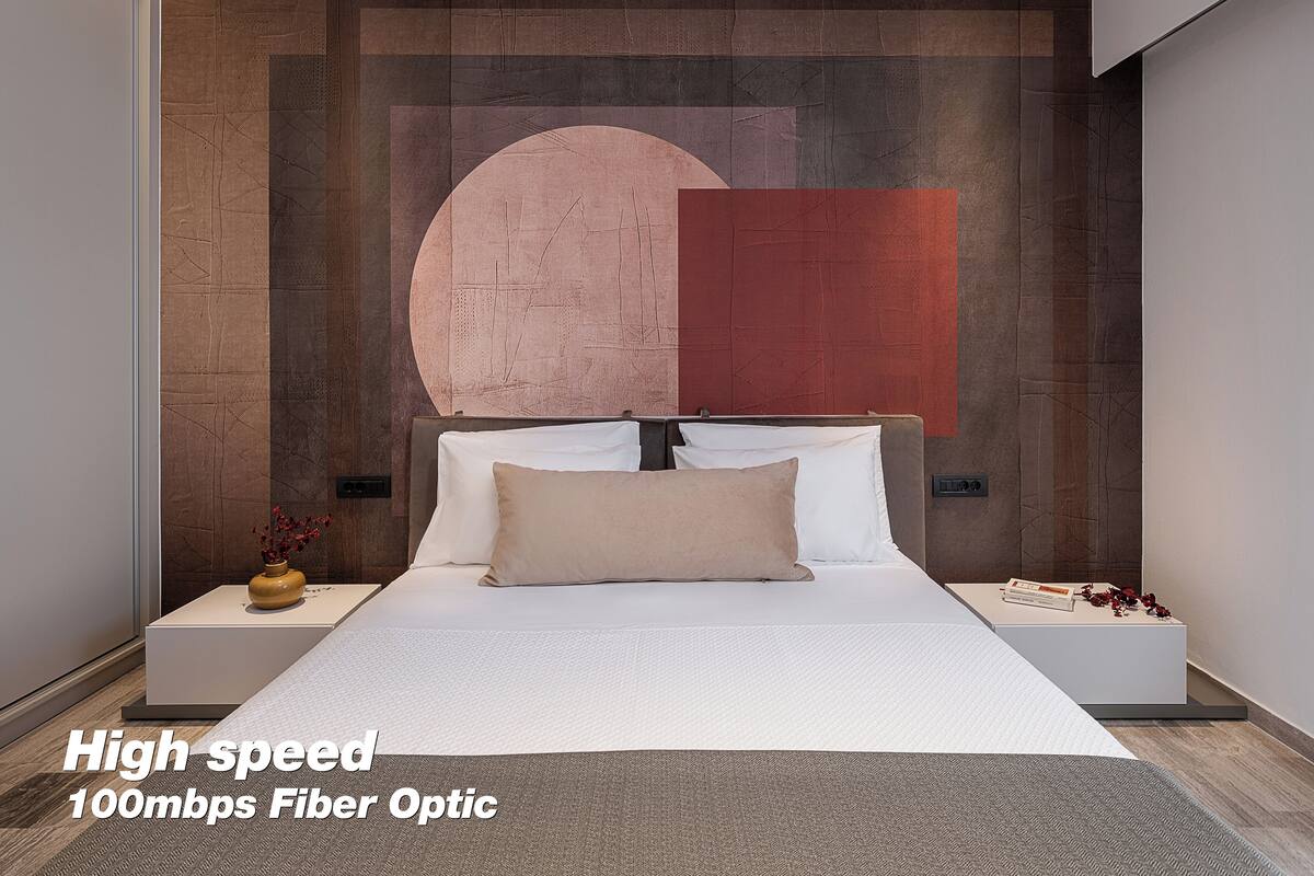 A modern bedroom with a large bed, a nightstand with a vase, and a wall with abstract art.