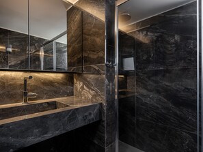 Ein modernes Badezimmer mit einer in Glas abgeschirmten Dusche, einem Marmorwaschbecken und einem großen Spiegel.