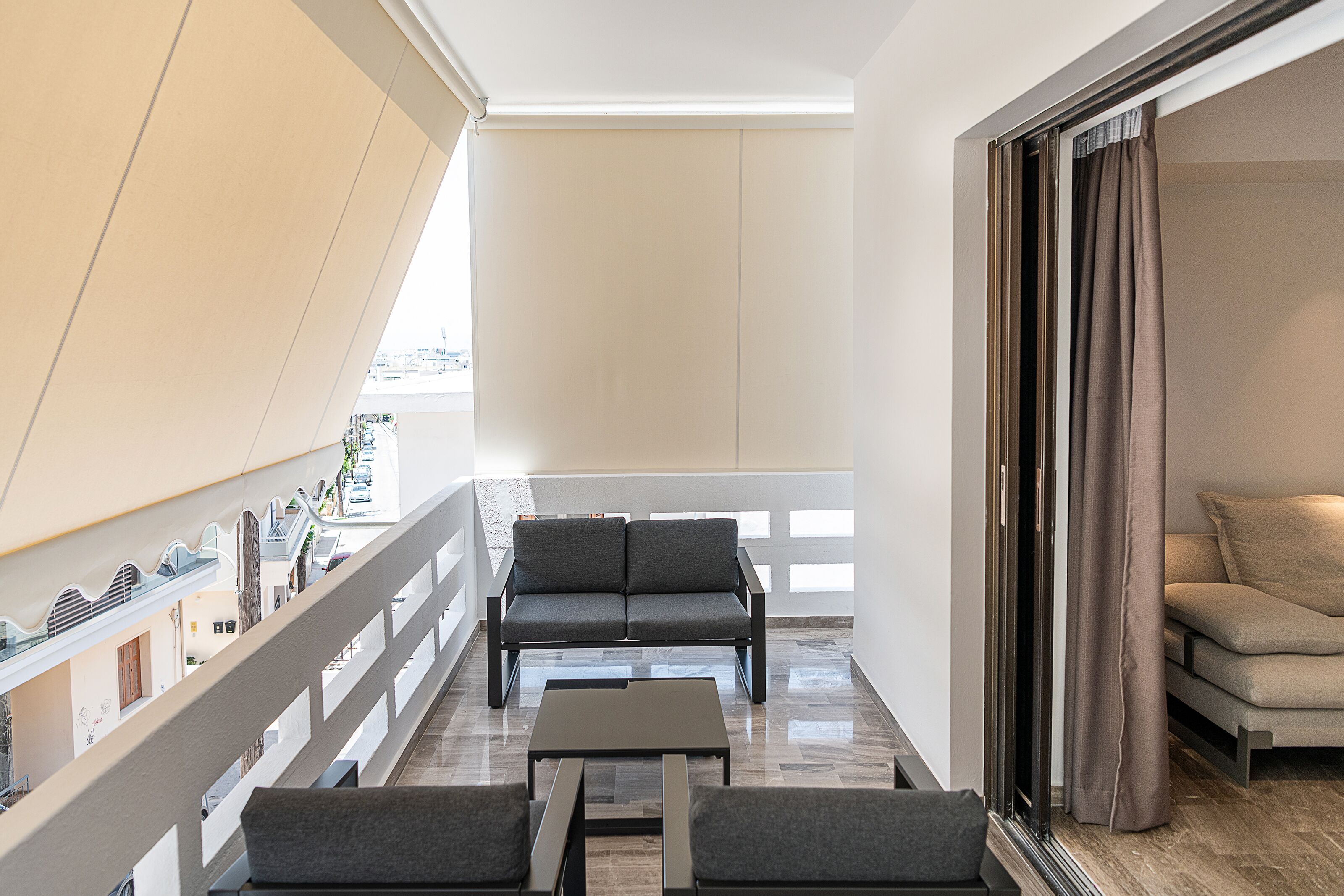 Een moderne hotelkamer met een balkon, een bank, een bijzettafeltje en uitzicht op de stad.
