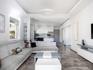 Ein modernes Wohnzimmer mit einem grauen Sofa, einem Couchtisch und einer Küche im Hintergrund.