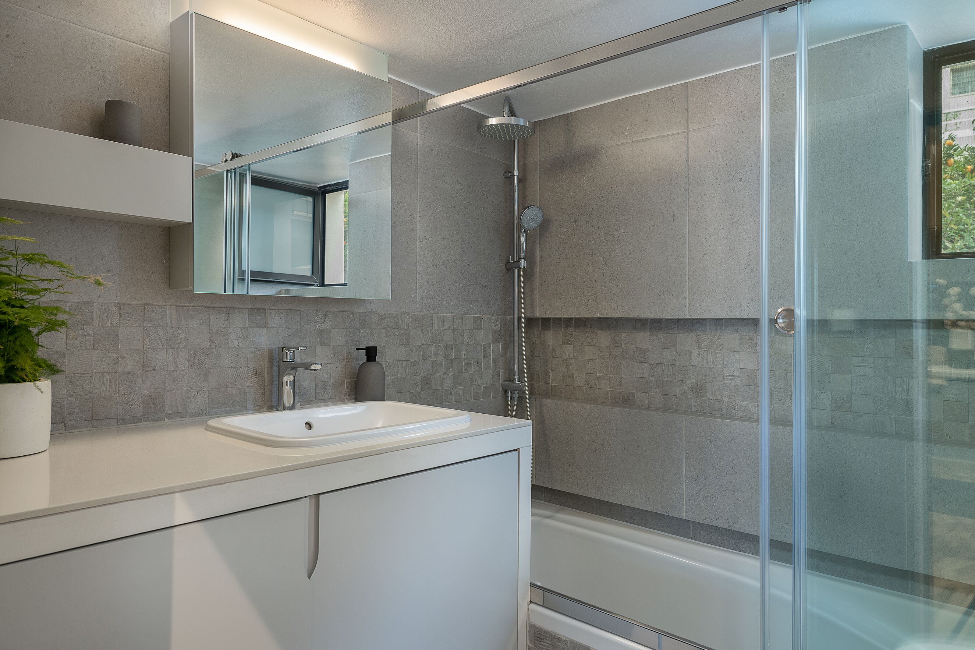 Un baño moderno con ducha envuelta en vidrio, un lavamanos blanco y un espejo grande sobre el mueble.