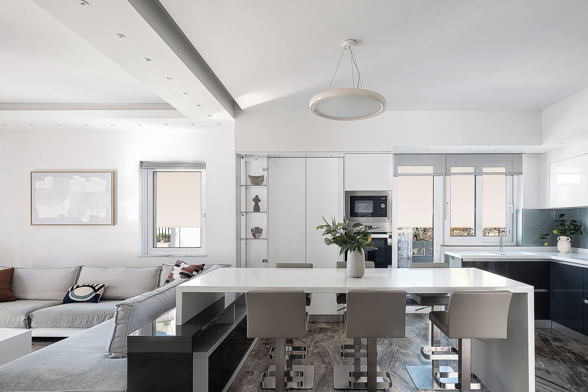 A modern kitchen with a central island, a dining area with bar stools, a sofa, and a TV.