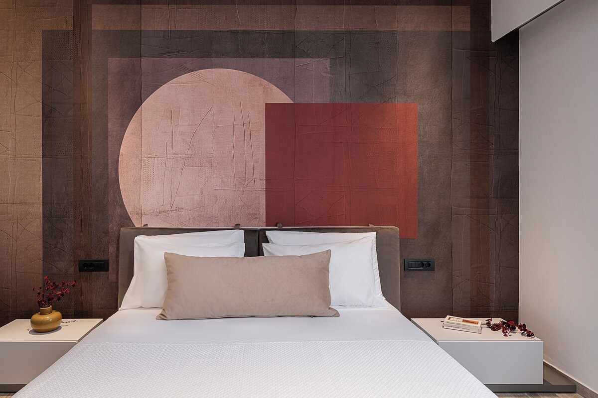 A modern bedroom with a large bed, a nightstand with a vase, and a wall with abstract art.