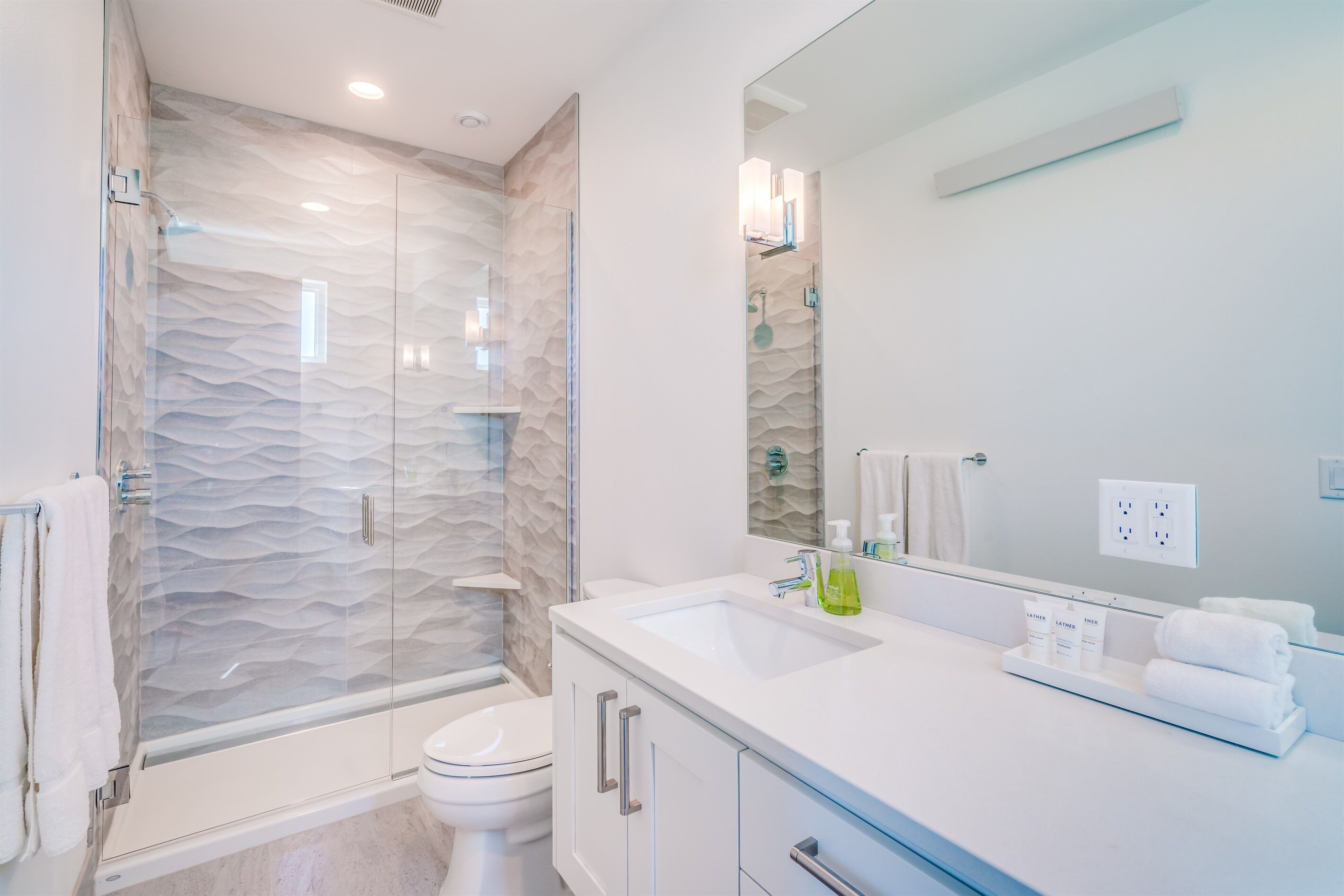 A modern bathroom with a glass-enclosed shower, a white sink, and a large mirror.