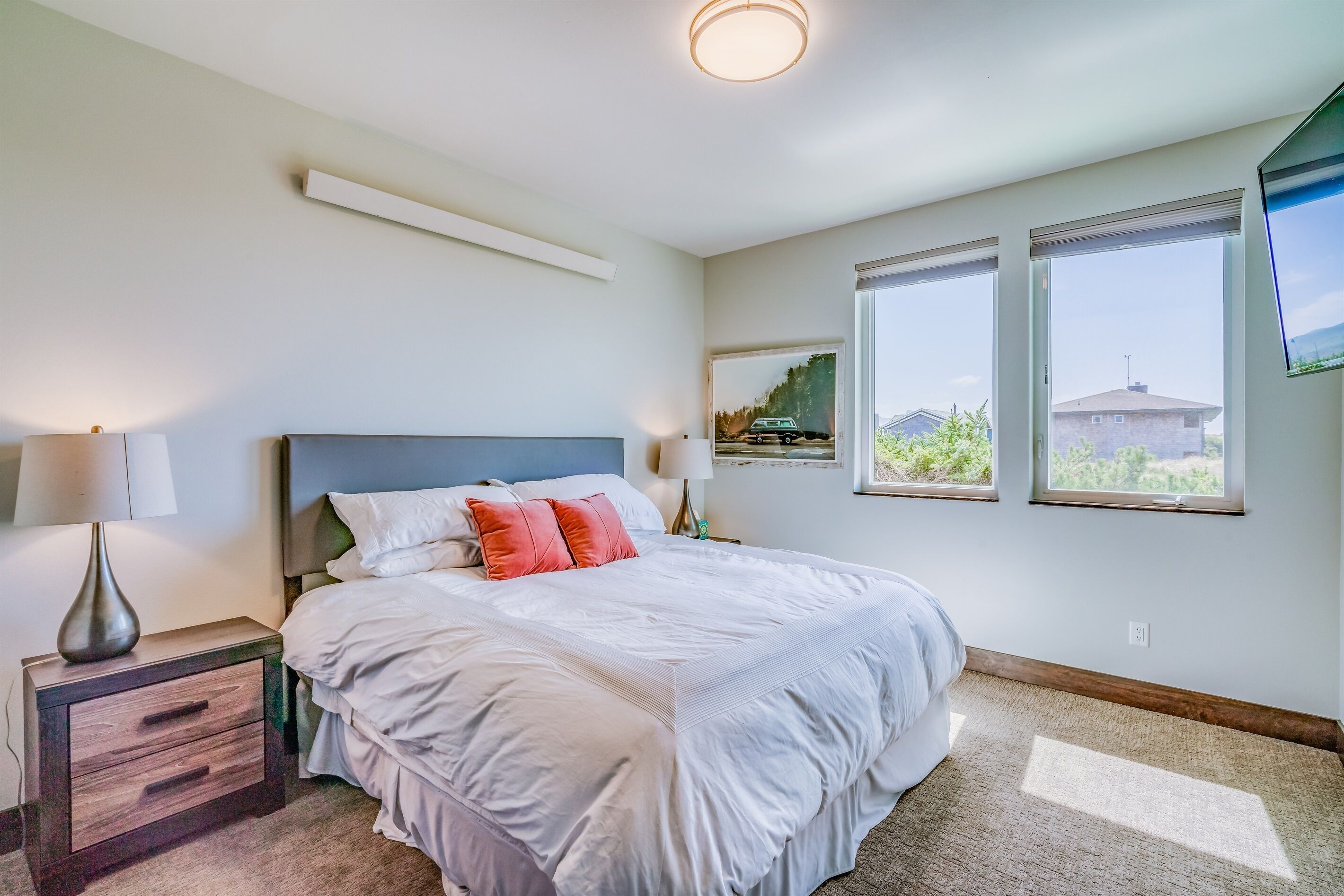 Un dormitorio con una cama grande, dos lámparas de noche, una mesita de noche y vistas al exterior a través de dos ventanas.