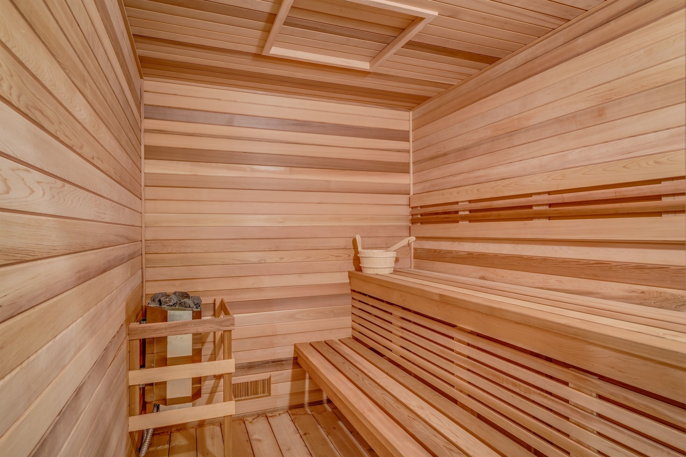 A wooden sauna with benches and a small shelf with a bucket and brush.