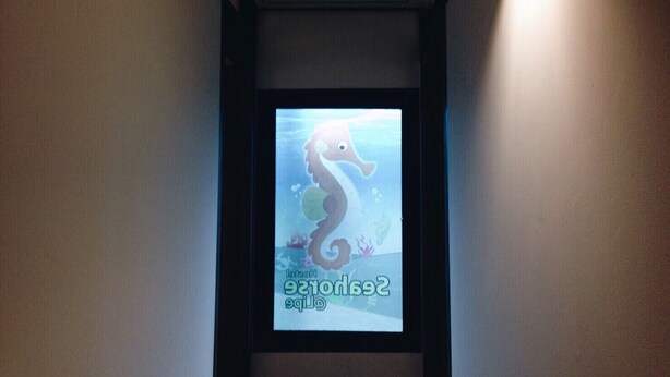 Un pasillo con una pantalla de proyección que muestra un personaje de caballito de mar y el texto "Seahorse Club".