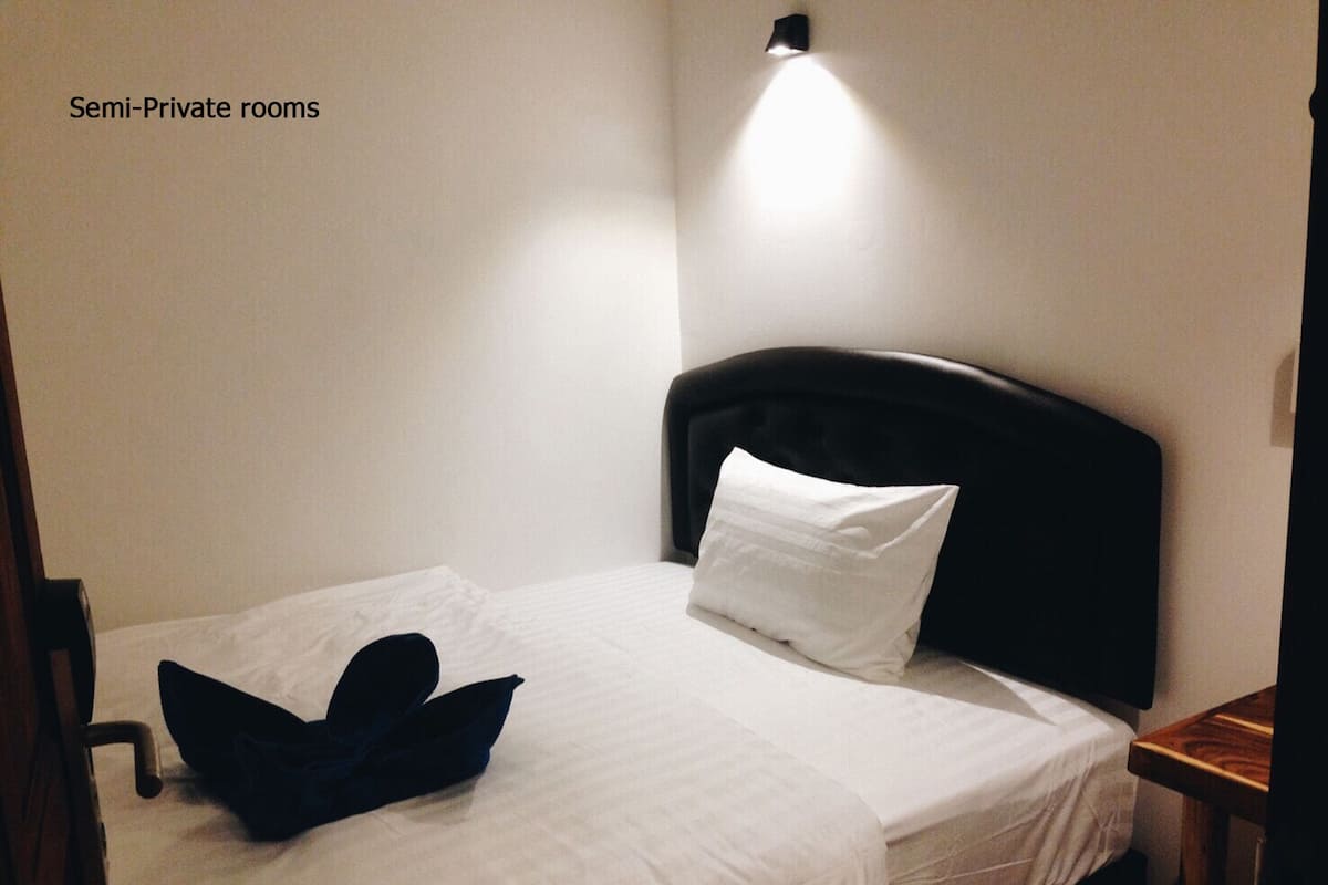 A semi-private room with a single bed, a pillow, a folded towel, and a nightstand.