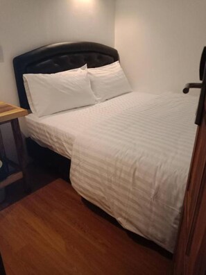 Een slaapkamer met een bed, nachtkastje en houten vloer.