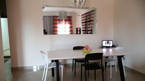 Un comedor con una mesa blanca, sillas blancas y negras, una computadora portátil sobre la mesa y un bol de fruta.