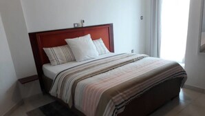Una cama bien hecha con una colcha a rayas y dos almohadas, un cabecero de madera y una mesita de noche pequeña.