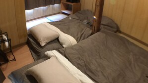 A room with two beds, each with a pillow and a blanket. There is a wooden nightstand with a television on it. - Ryokan Nakadaya (Tokyo)