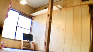 A tatami mat room with a television, wooden walls, and a large window. - Ryokan Nakadaya (Tokyo)
