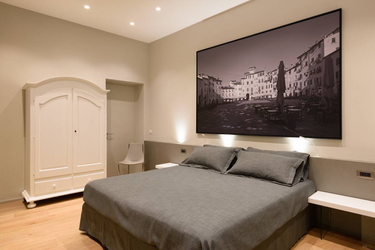 Ett sovrum med en stor säng, en garderob, ett skrivbord och en väggmonterad tv som visar en stadsbild.