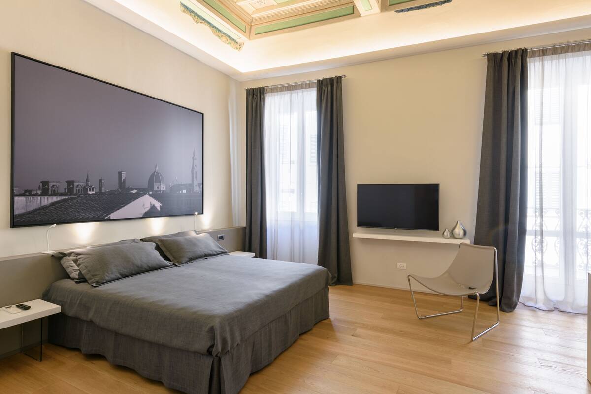 Ett modernt sovrum med en stor säng, en platt-TV och en tavla med en stadsbild på väggen.