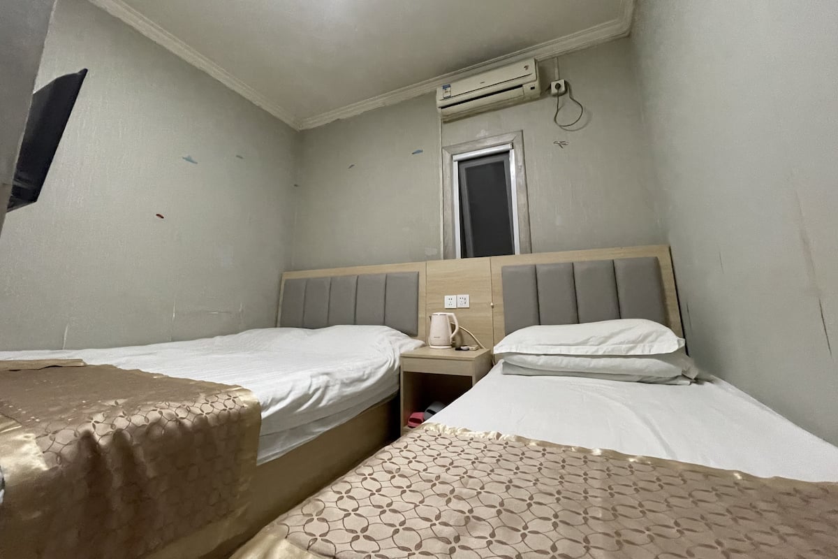 Une chambre d’hôtel avec deux lits, une fenêtre, un appareil de climatisation et une table de chevet avec une lampe.