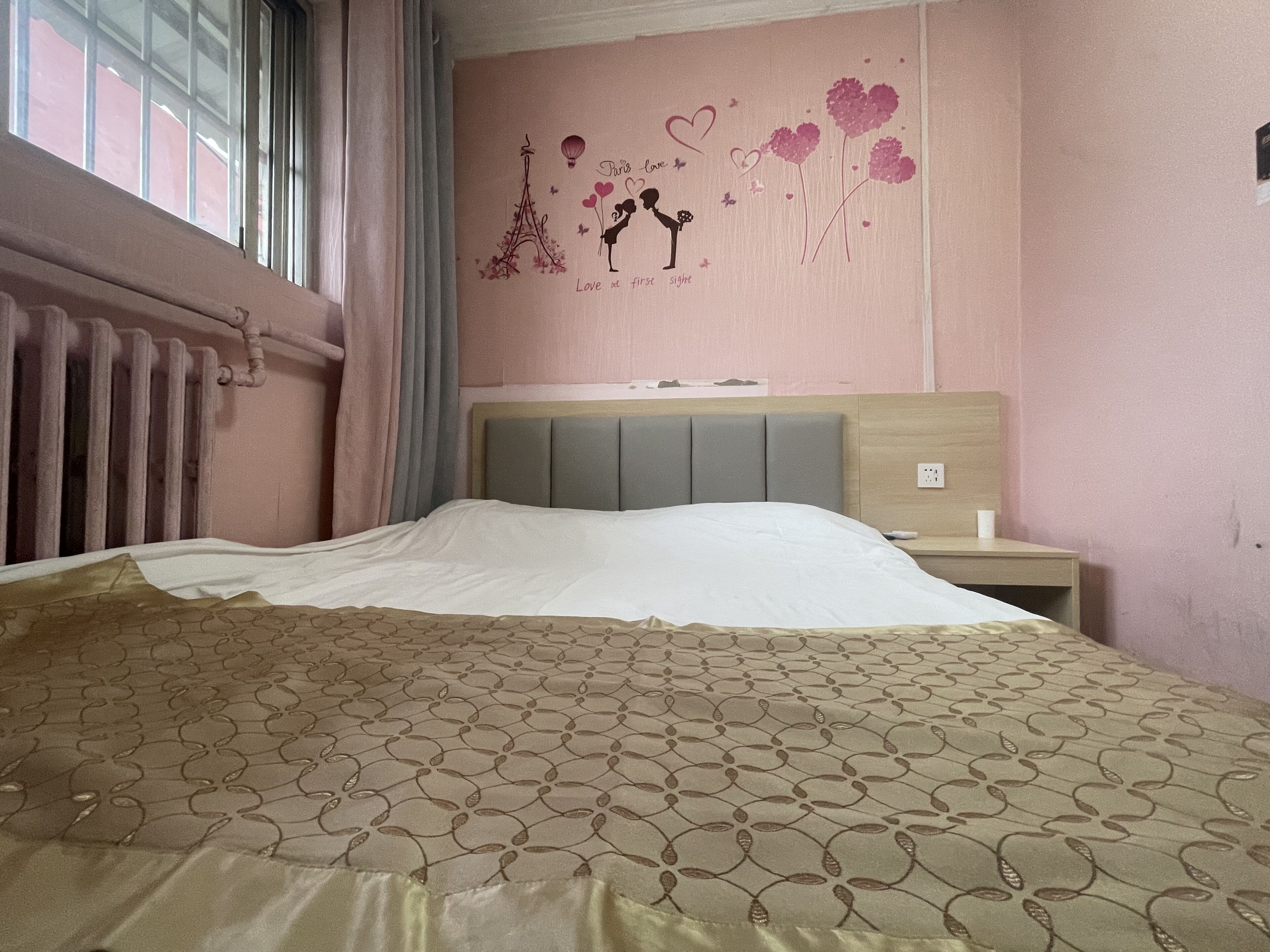 A bedroom with a bed, a nightstand, a wall with a decorative mural, and a window with curtains.