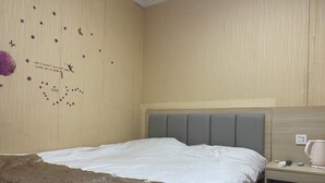 A neatly made bed with a grey headboard, a bedside table with a lamp, and a wall with a floral pattern and a heart-shaped arrangement of stars and flowers. - Beijing Huairou Pan Jia Yuan Hotel (Huairou)