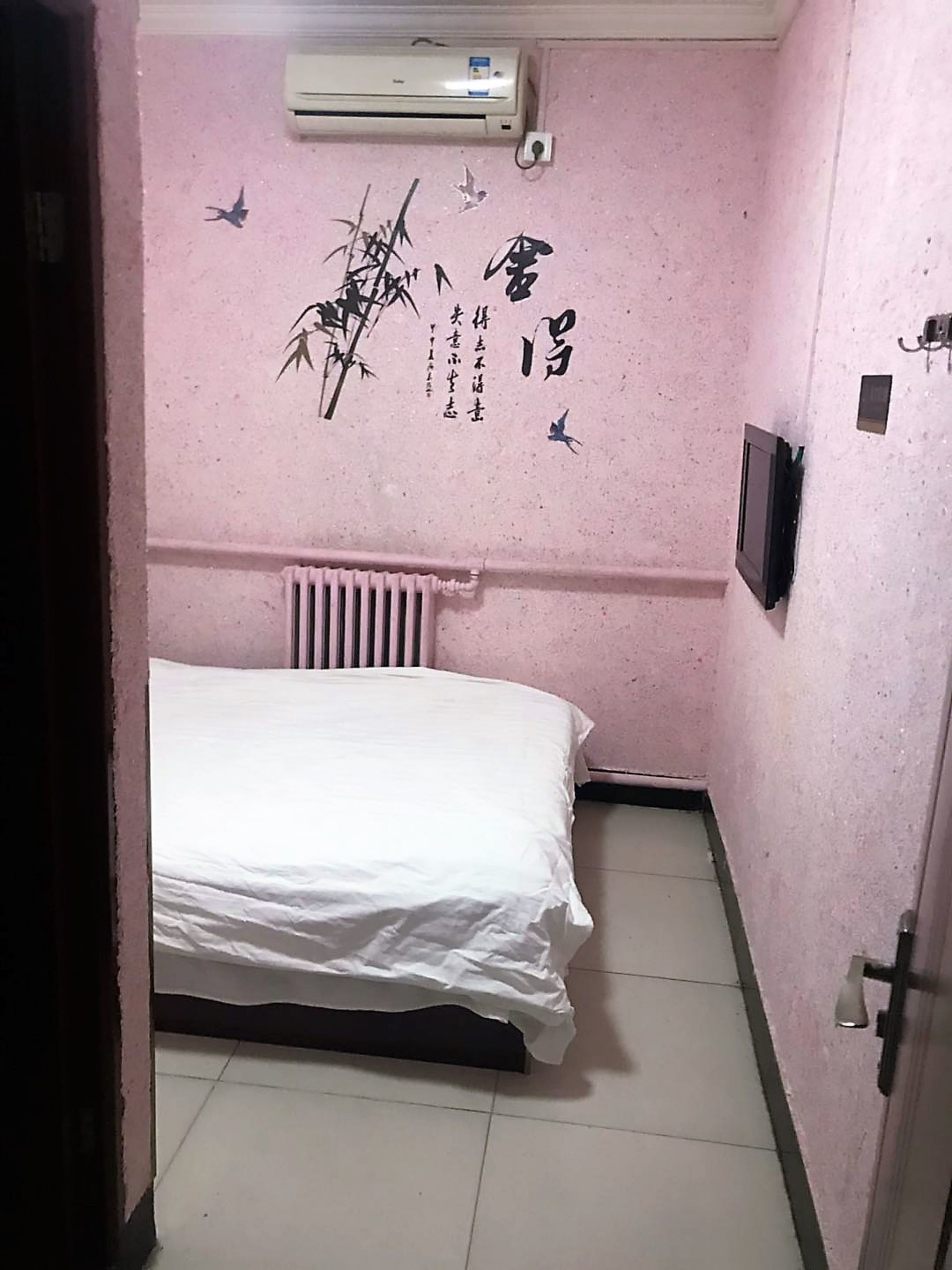A small, pink-walled bedroom with a white bed, a radiator, and a wall-mounted TV.