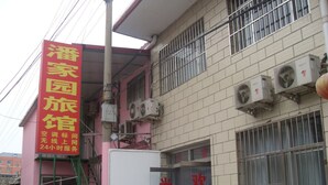 A building with a pink exterior and a signboard with yellow text. There are air conditioning units on the wall and a staircase leading to the entrance. - Beijing Huairou Pan Jia Yuan Hotel (Huairou)