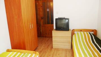 Une chambre avec deux lits simples, une armoire en bois, un téléviseur posé sur une petite table et une porte donnant sur une autre pièce.