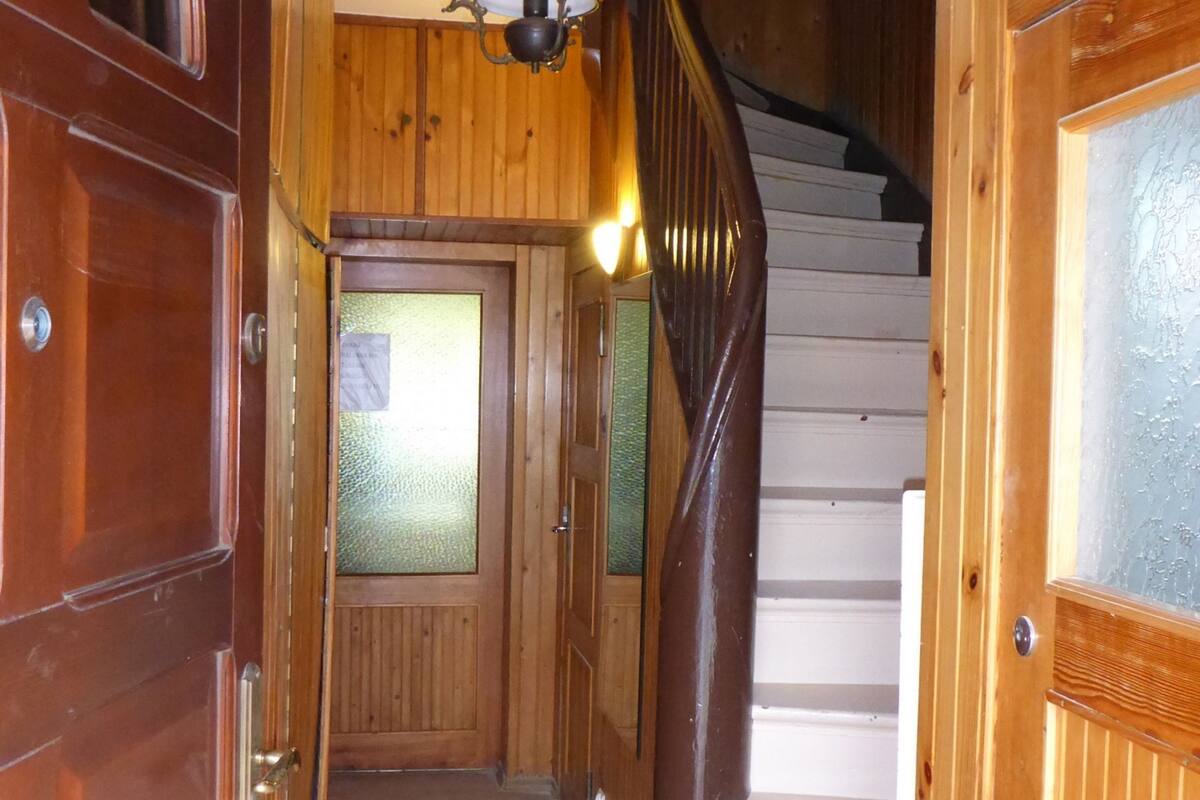 Un intérieur en bois comprenant un escalier, un couloir et une porte dotée de panneaux en verre dépoli.