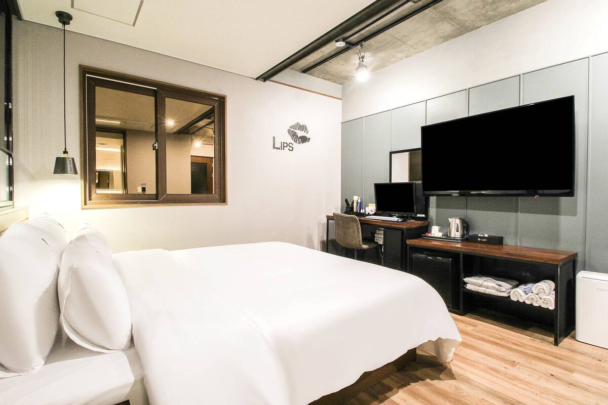 A hotel room with a bed, desk, chair, TV, and a mirror.