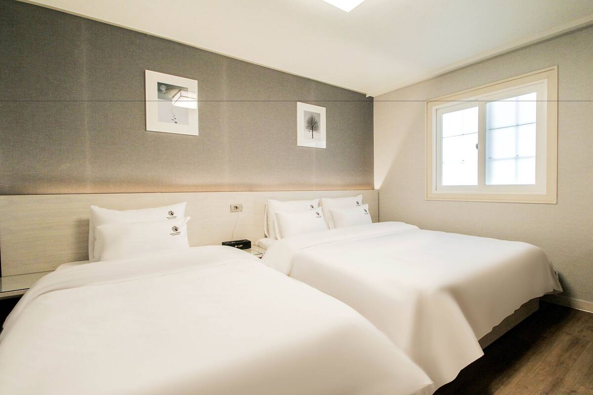 A hotel room with two beds, a large window, and a wall-mounted artwork.