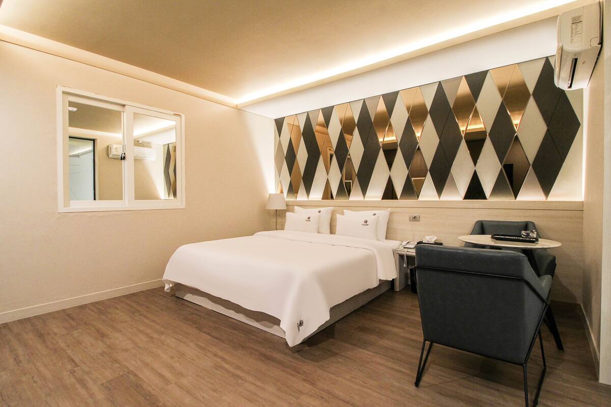 A hotel room with a bed, a desk, a chair, and a mirror.