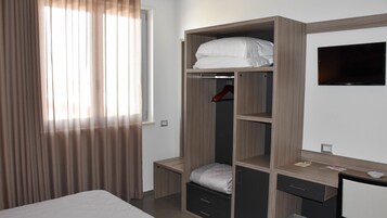 Un dormitorio con cama, armario con estantes, escritorio y televisor.