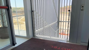 Entrada de un hotel con una reja metálica, un felpudo con la inscripción 'SOSTA' y 'MOTEL', y vistas a un paisaje desértico.