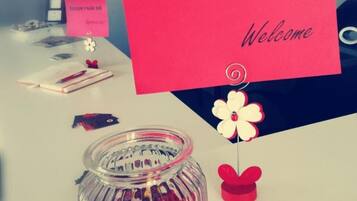 Una recepción con un cartel de 'Bienvenue Welcome', un tarro de caramelos y una pequeña decoración floral.