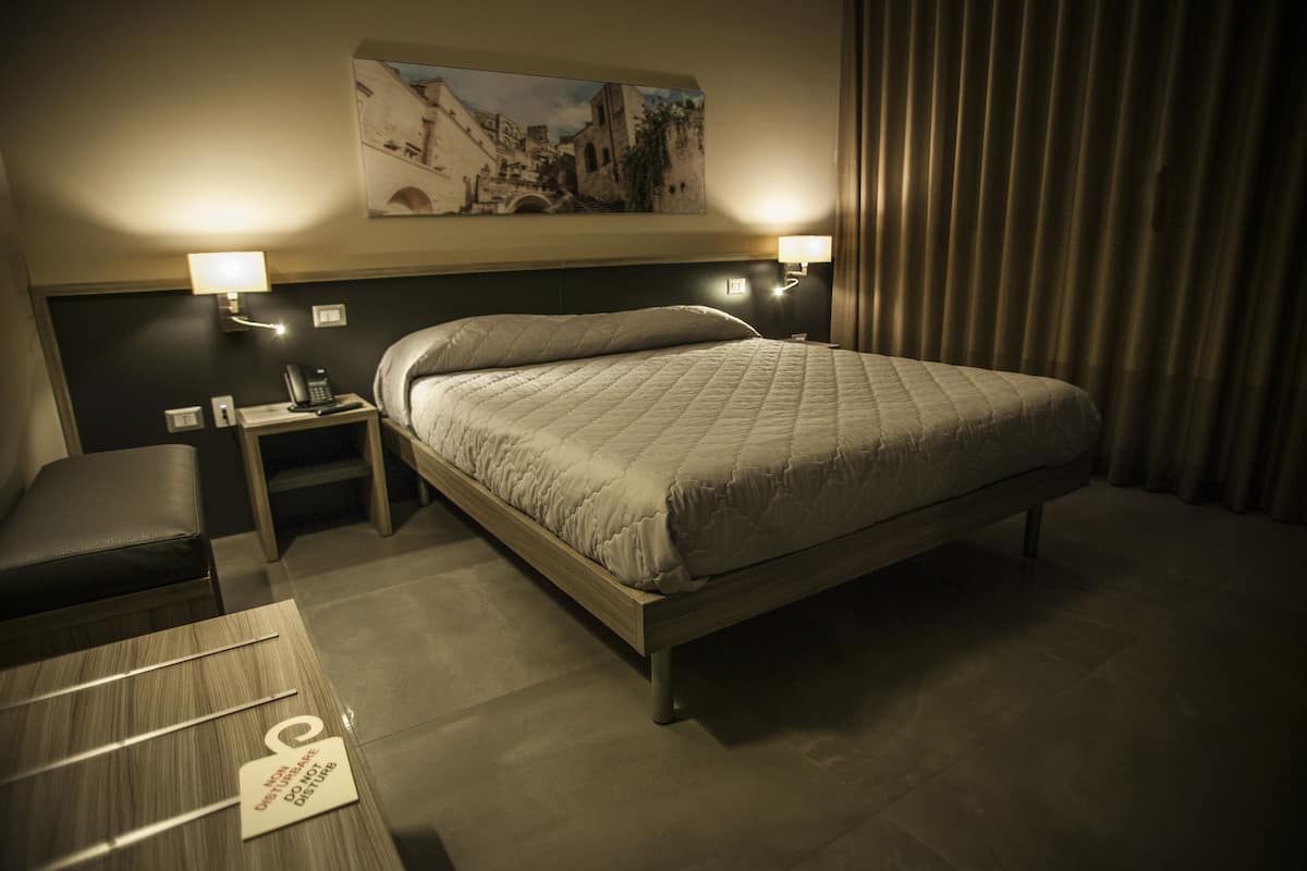A hotel room with a bed, bedside tables, a nightstand with a phone, and a painting on the wall.