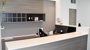 Un mostrador de recepción moderno con una combinación de colores gris y blanco, un estante de madera encima y un pequeño jarrón con flores.